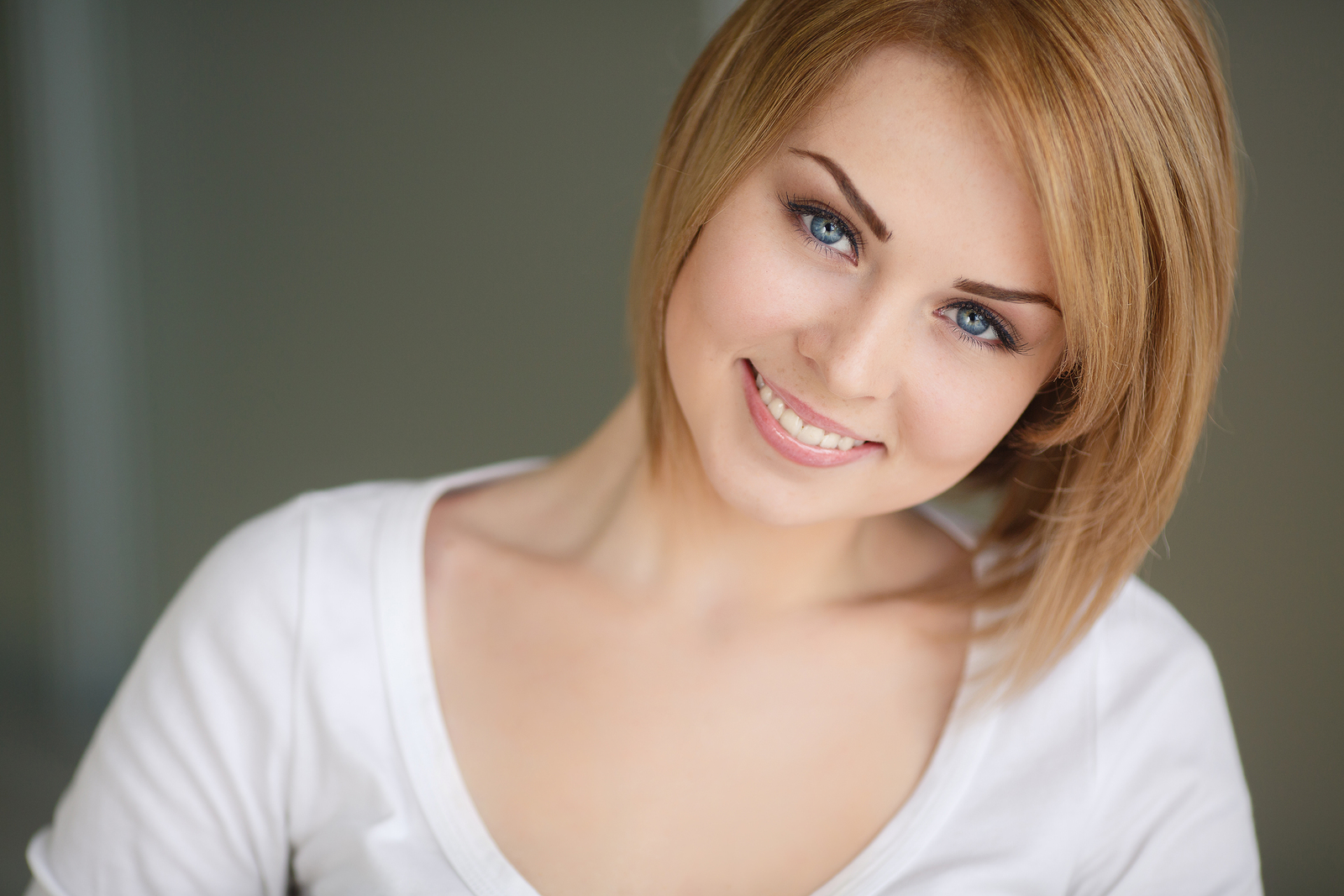 A beautiful portrait of a fair-haired young woman with beautiful hair,grey eyes,sweet smile and beautiful eyebrows,dressed in a white t-shirt with a deep neckline,isolated on a gray background.
